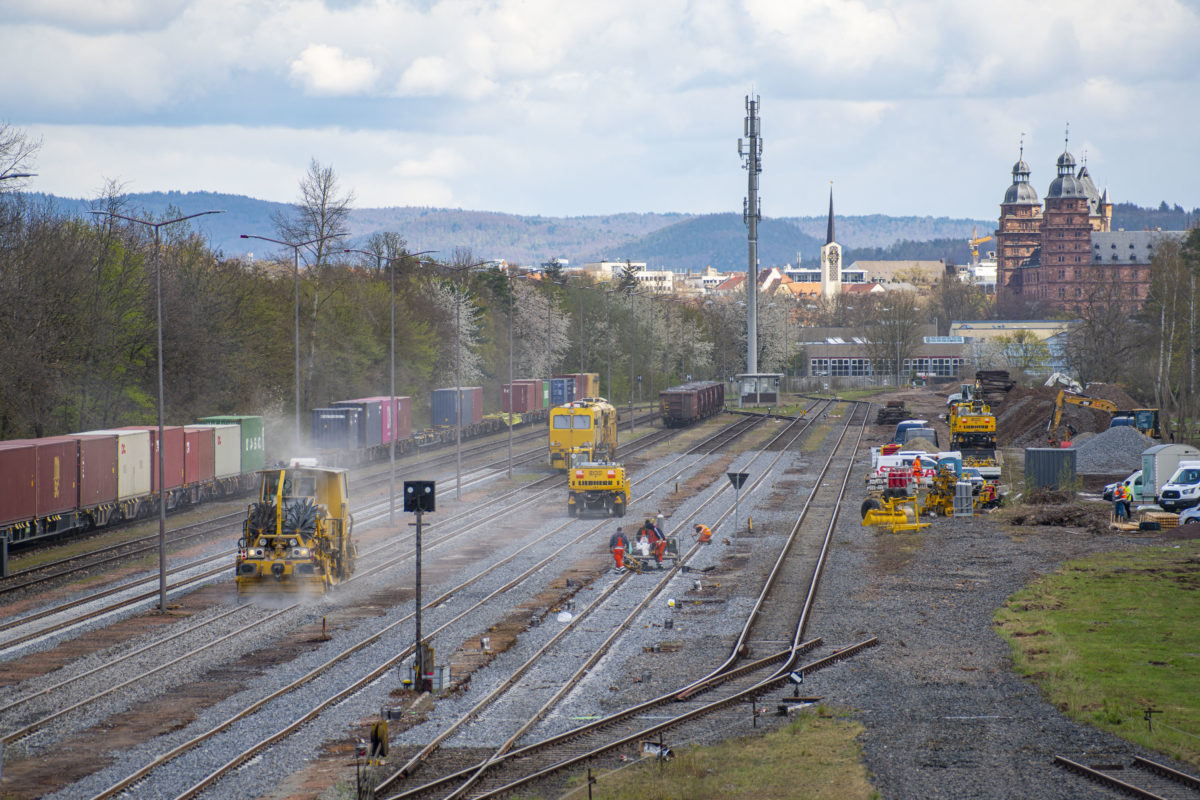 Hafenbahnhof Aschaffenburg rechts Bauarbeiten mit Gleisstopfzug, links durchfahrender Containerzug